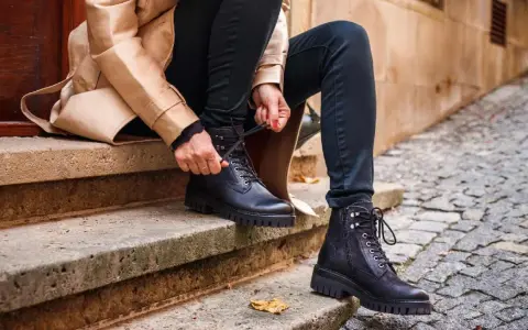Persona se sienta en escalones de piedra, atándose unos pantalones anchos con botas militares negras.