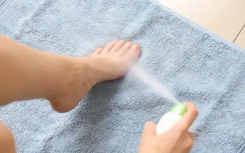 Persona rocía spray refrescante en sus pies cocidos sobre una toalla azul.