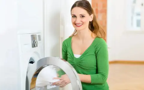 Mujer sonriente carga sábanas en lavadora. El programa para lavar sábanas es fácil de usar.