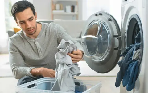 Hombre saca ropa de la lavadora, preocupado por la ropa que destiñe en la piel.