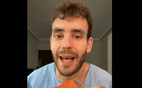 Hombre con bata azul muestra una zapatilla naranja, recordando que los pies crecen con la edad.