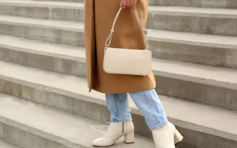 Mujer con abrigo camel, jeans y bolso crema, lista para combinar outfit con botas beige.