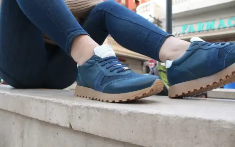 Un hombre luce unas zapatillas azules con cordones y suela de goma, combinadas con vaqueros oscuros.