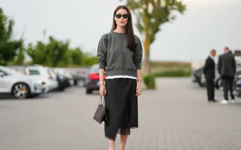 Mujer con falda satinada y zapatillas, bolso marrón y gafas de sol.