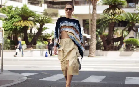 Mujer con un top corto de crochet y una falda vaporosa color beige, paseando por la calle con palmeras de fondo.