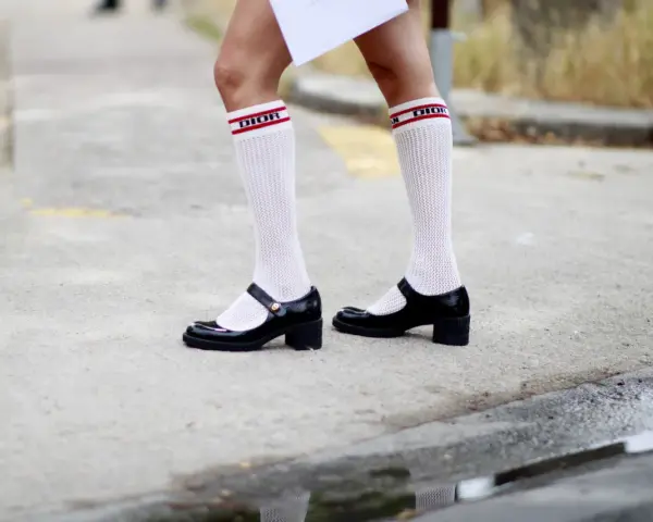 Merceditas negras con calcetines blancos de rejilla y banda roja con logo "DIOR", un look infantil y chic.
