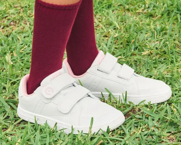 Niño con calcetines granates y zapatillas blancas con velcro, listas para limpiar y jugar en el césped.