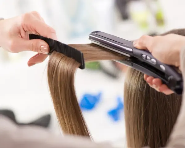 Manos peinando y alisando cabello con una plancha. ¡Sorprendentemente, se puede planchar la ropa con la plancha del pelo!