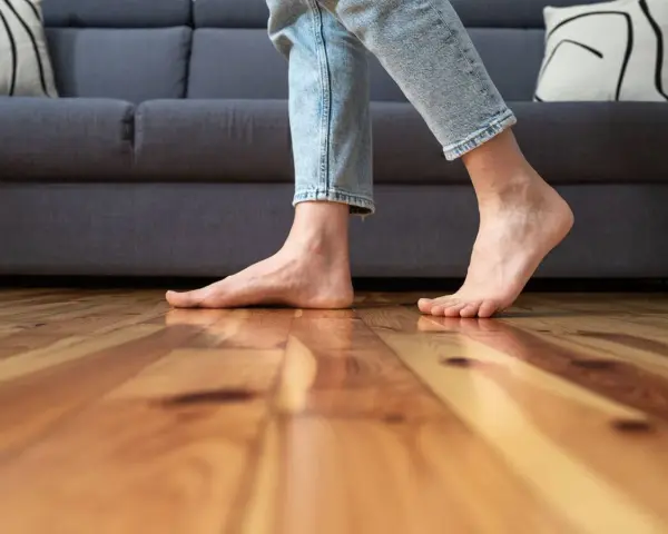 Pies descalzos sobre suelo de madera, sintiendo el frío al caminar cerca del sofá.