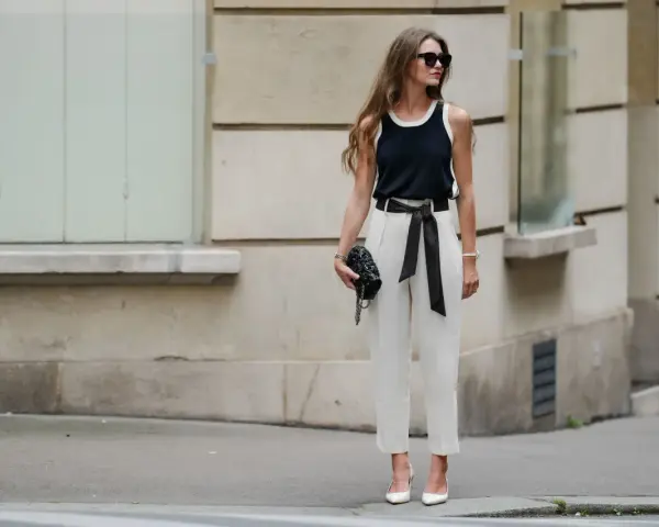 Mujer con elegante pantalón lino blanco, top negro y bolso de mano, posando con confianza.