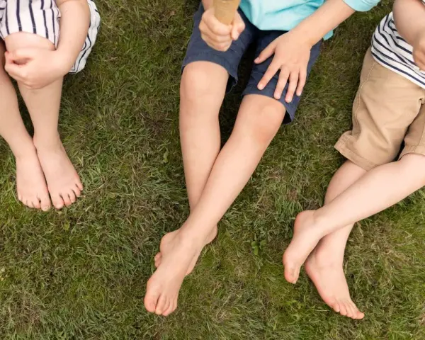 Niños sentados en el césped, uno con shorts talla 28 niño, disfrutando de un helado.