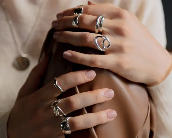 Manos adornadas con varios anillos de plata, uno de ellos con un diseño que recuerda a un anillo de flor.