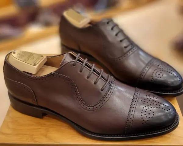 Elegantes zapatos de vestir marrones con puntera de cap toe y perforaciones. La talla UK se convierte a EU para un ajuste perfecto.