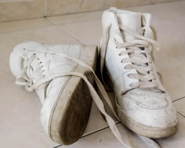 Par de zapatillas blancas sucias, con cordones desatados, sobre baldosas. Aprende como secar zapatillas blancas para que no se pongan amarillas.
