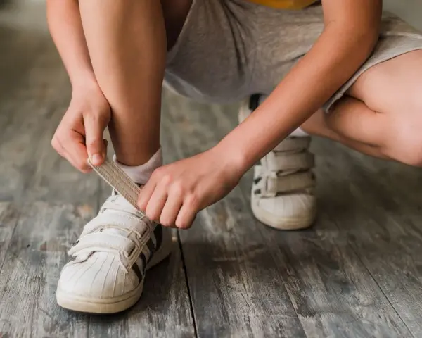 Niño se ata los cordones de sus zapatillas blancas. El número de pie según edad cambia rápido, ¡hay que estar al día!