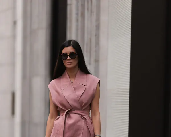 Mujer con gafas de sol y un elegante chaleco de lino rosa, atado a la cintura, pasea por la ciudad.