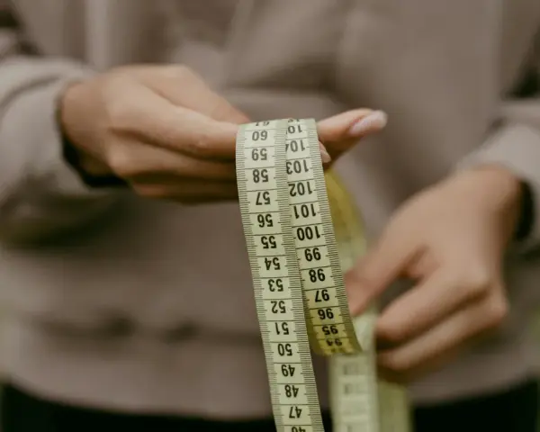 Manos sostienen cinta métrica. La talla 36 UK es un objetivo, pero la cinta muestra medidas en centímetros.