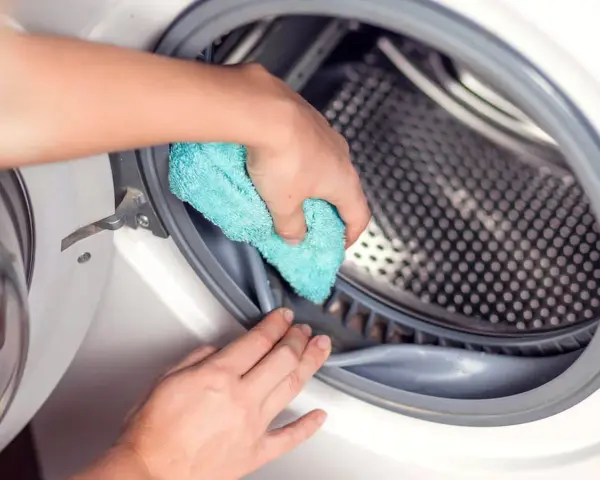 Mano limpiando la goma de la lavadora con un paño azul. Un paso esencial para saber como desinfectar una lavadora usada.