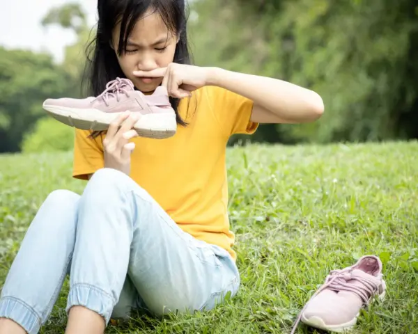 Niña con cara de asco huele un zapato, quizás por el sudor de los pies de niños tras un día de juegos.