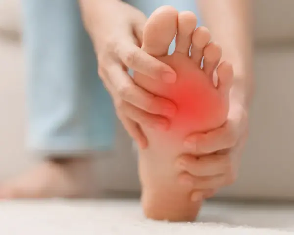 Persona se toca la almohadilla del pie, con una zona roja indicando dolor. Busca remedios caseros para el dolor en la almohadilla del pie.