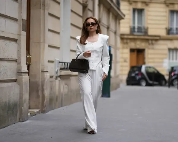 Mujer con un elegante traje blanco, destacando su pantalón ibicenco de corte ancho, camina por una calle parisina.