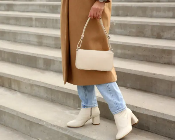 Mujer con abrigo camel, jeans y bolso crema, lista para combinar outfit con botas beige.