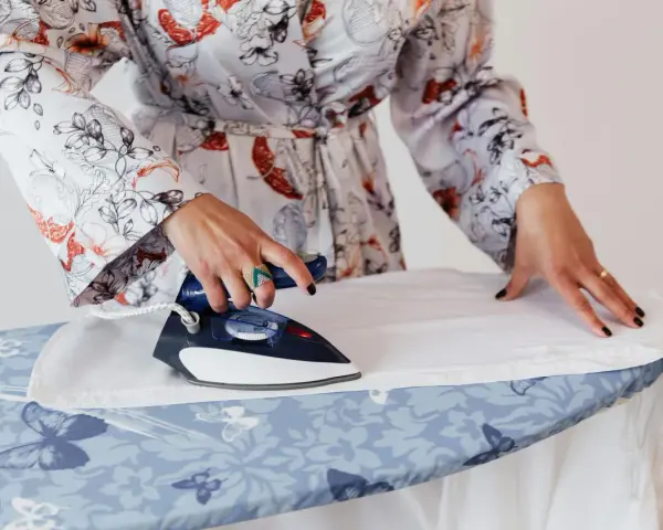 Mujer con bata estampada plancha lino blanco a mano sobre tabla con mariposas.