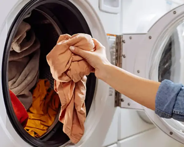 Mano saca ropa de lavadora. Es hora de limpiar lavadora a 90 grados para desinfectarla.