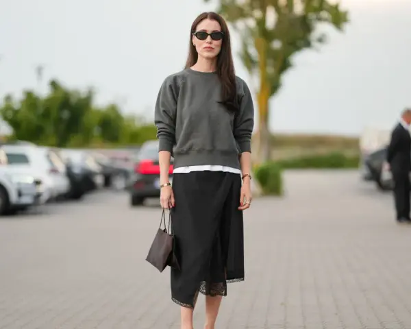 Mujer con falda satinada y zapatillas, bolso marrón y gafas de sol.