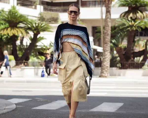 Mujer con un top corto de crochet y una falda vaporosa color beige, paseando por la calle con palmeras de fondo.