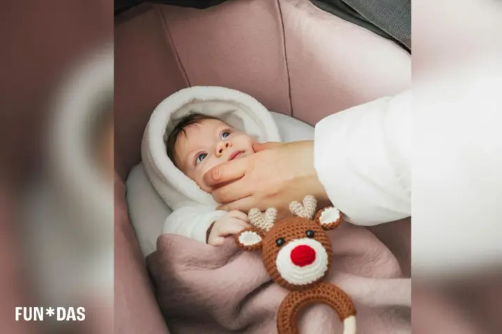 Bebé recién nacido envuelto en manta rosa, con un peluche de reno. Una mano le acaricia la mejilla, como si fuera a poner calcetines a los bebé recién nacido.