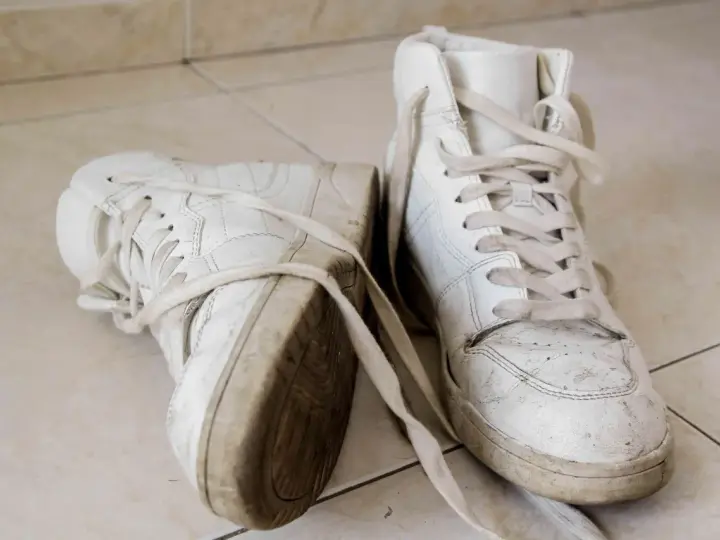 Par de zapatillas blancas sucias, con cordones desatados, sobre baldosas. Aprende como secar zapatillas blancas para que no se pongan amarillas.