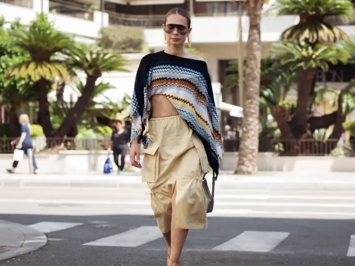 Mujer con un top corto de crochet y una falda vaporosa color beige, paseando por la calle con palmeras de fondo.