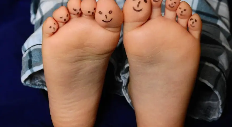 Caritas sonrientes en los dedos de bebés descalzos en invierno, jugando con sus pies.