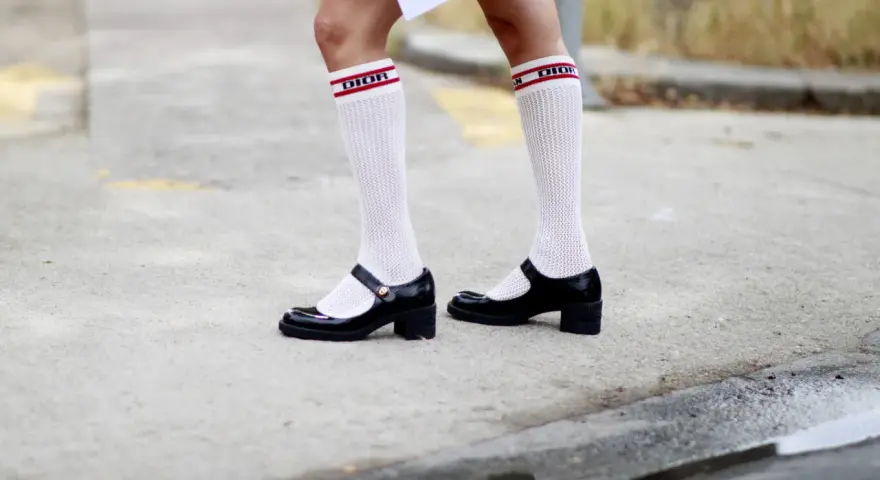 Merceditas negras con calcetines blancos de rejilla y banda roja con logo "DIOR", un look infantil y chic.