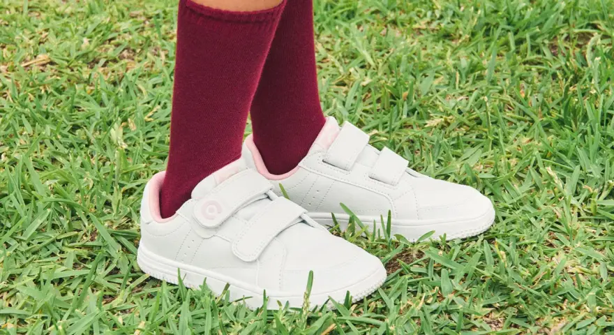 Niño con calcetines granates y zapatillas blancas con velcro, listas para limpiar y jugar en el césped.