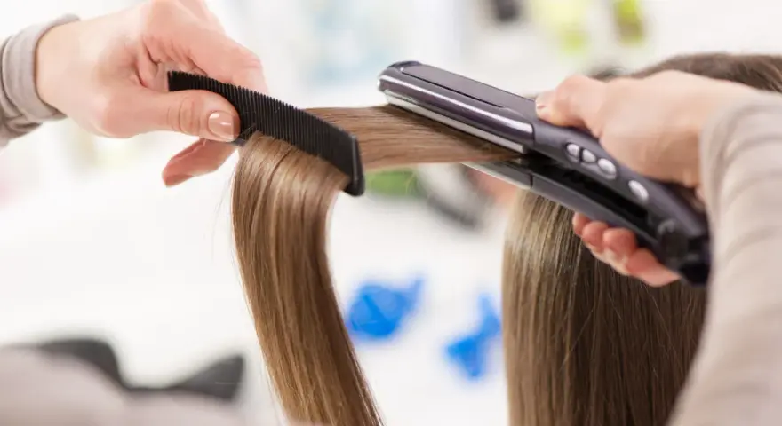Manos peinando y alisando cabello con una plancha. ¡Sorprendentemente, se puede planchar la ropa con la plancha del pelo!