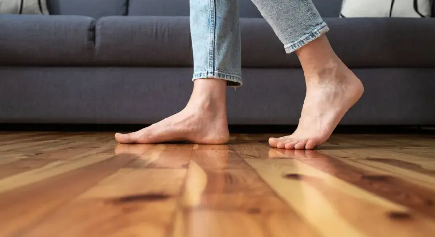Pies descalzos sobre suelo de madera, sintiendo el frío al caminar cerca del sofá.