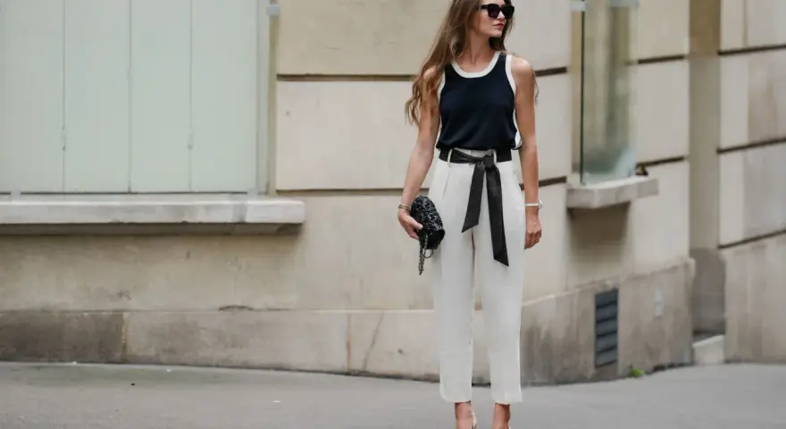 Mujer con elegante pantalón lino blanco, top negro y bolso de mano, posando con confianza.