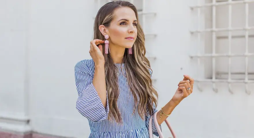 Mujer con un vestido de rayas azules y blancas, mangas acampanadas y pendientes rosas.