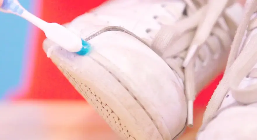Cepillo dental azul y blanco limpia la suela de unas zapatillas blancas. Un truco para saber como limpiar las suelas de las zapatillas de casa.
