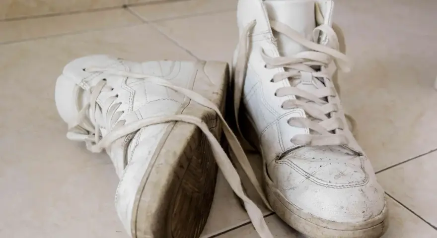 Par de zapatillas blancas sucias, con cordones desatados, sobre baldosas. Aprende como secar zapatillas blancas para que no se pongan amarillas.