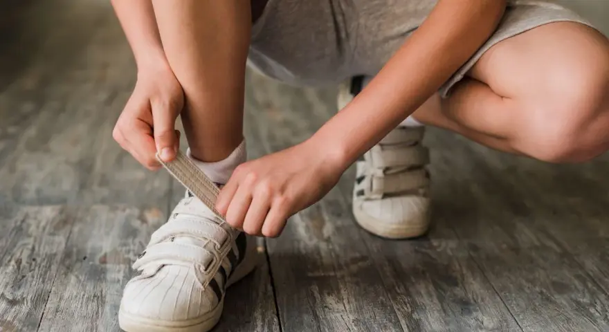 Niño se ata los cordones de sus zapatillas blancas. El número de pie según edad cambia rápido, ¡hay que estar al día!