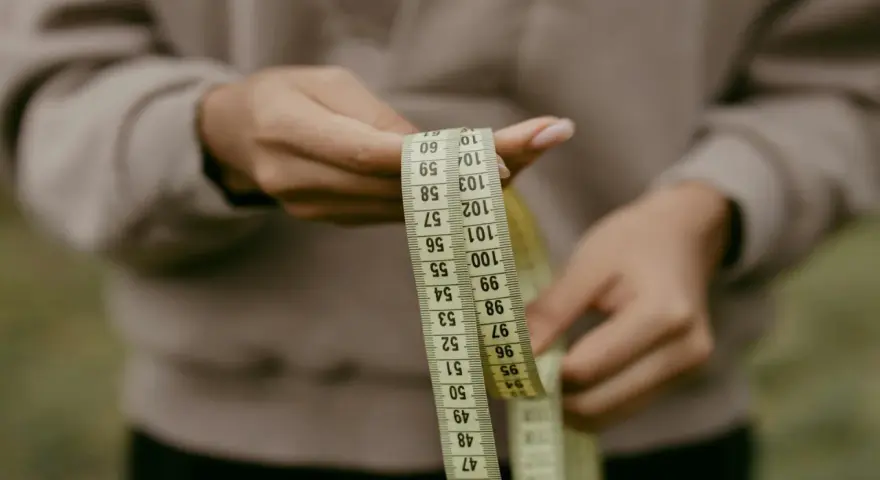 Manos sostienen cinta métrica. La talla 36 UK es un objetivo, pero la cinta muestra medidas en centímetros.