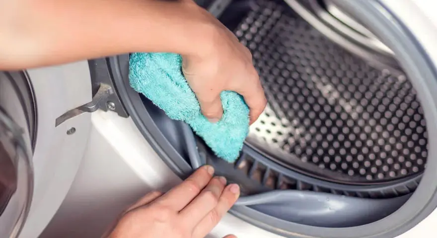 Mano limpiando la goma de la lavadora con un paño azul. Un paso esencial para saber como desinfectar una lavadora usada.