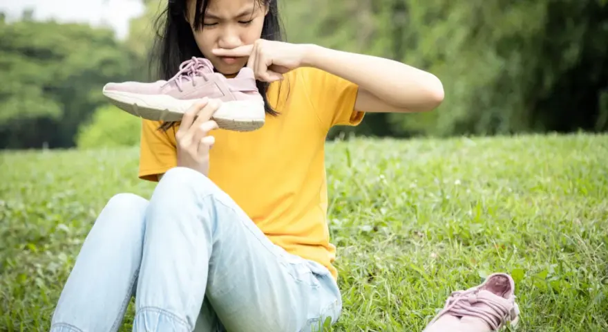 Niña con cara de asco huele un zapato, quizás por el sudor de los pies de niños tras un día de juegos.
