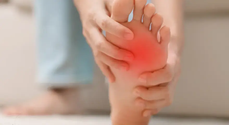 Persona se toca la almohadilla del pie, con una zona roja indicando dolor. Busca remedios caseros para el dolor en la almohadilla del pie.