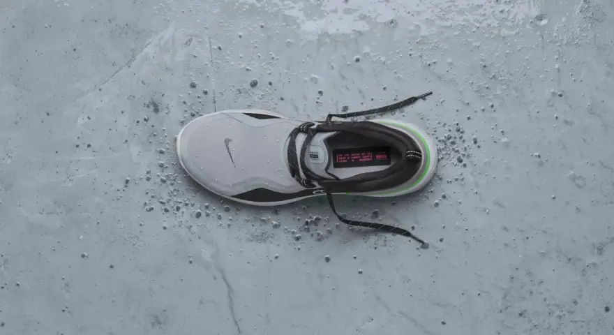 Zapatilla Nike gris con detalles verdes y negros, mojada y con gotas de agua. ¡Perfecta para que se puedan meter las zapatillas en la secadora sin problema!