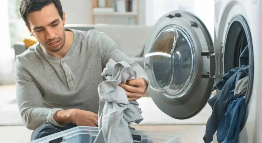 Hombre saca ropa de la lavadora, preocupado por la ropa que destiñe en la piel.