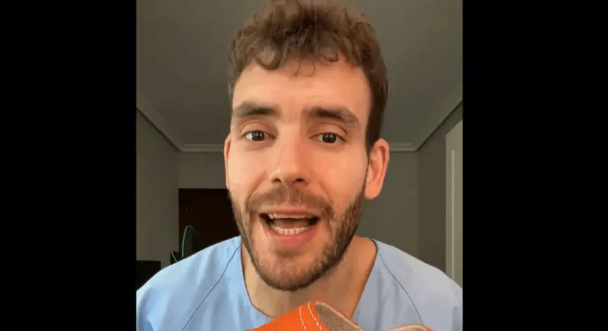 Hombre con bata azul muestra una zapatilla naranja, recordando que los pies crecen con la edad.